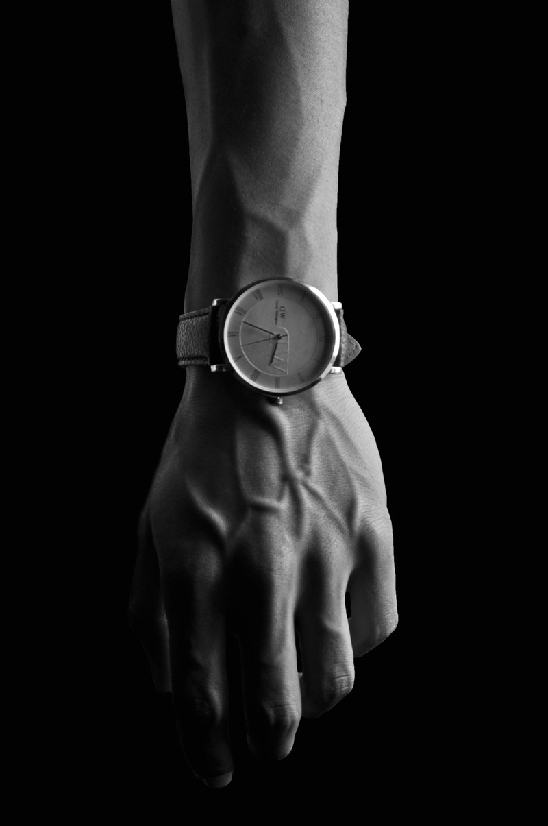 A round analogue watch on a wrist, side-lit, black and white.