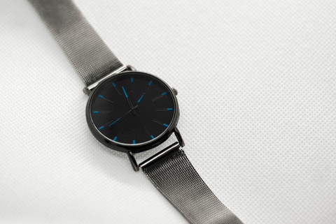 A black-dial watch on a steel mesh strap.
