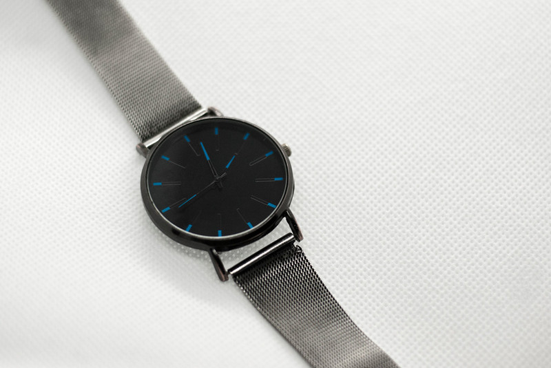 A black-dial watch on a steel mesh strap.