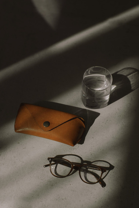 Glasses, a tan leather case and a glass of water in raking light.